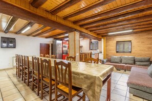 Un espace repas avec une longue table en bois et des chaises, une cuisine en arrière-plan et un coin salon avec un canapé.