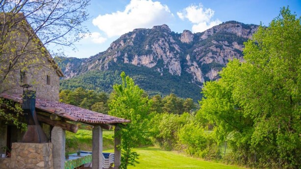 A stone building with a tiled roof, a covered outdoor seating area, and a view of a mountainous landscape. - Country House 'Can Caubet Lll' with Mountain View, Shared Pool and Wi-Fi (Capolat)