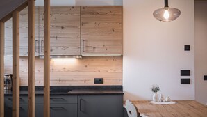 A modern kitchen with wooden cabinets, a black countertop, and a wooden dining table with a vase.