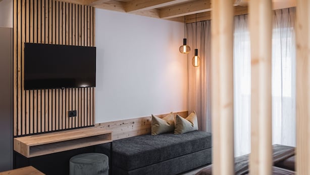 A modern room with a flat-screen TV mounted on a wooden slat wall, a grey sofa with cushions, and two pendant lights.
