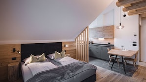 A modern bedroom with a large bed, a wooden headboard, and a small kitchen area with a dining table.