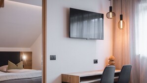 Una habitación de hotel con cama, escritorio con dos sillas, televisor montado en la pared y dos lámparas colgantes.