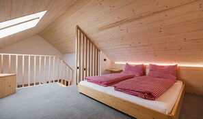 Quarto em estilo loft com teto inclinado, uma cama de madeira, uma pequena escrivaninha e uma escada.