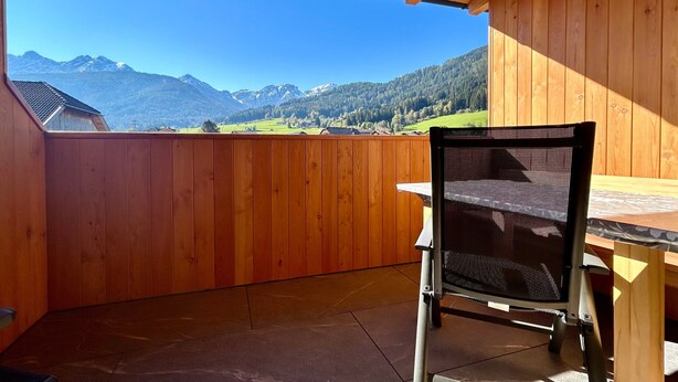 Un balcón de madera con vistas a montañas, una silla y una mesa.