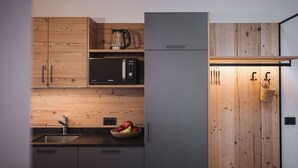 Una cocina con armarios de madera, microondas, hervidor, pileta y frutero.