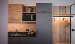 A kitchen with wooden cabinets, a microwave, a kettle, a sink, and a fruit bowl.