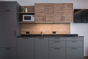 Et moderne køkken med grå skabe, en træbeklædt bagvæg, en mikroovn og en stålvask.