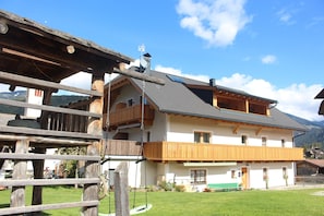 A two-story building with a balcony, a wooden fence, and a grassy yard.