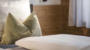 A bed with pillows, a bedside table with a lamp, wooden paneling on the wall, and a window with curtains.