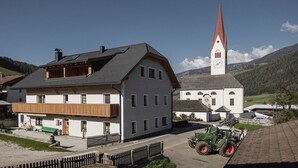 A two-story building with a balcony, a church with a tall steeple, and a tractor in the foreground.