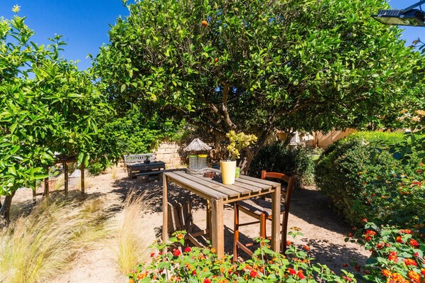 A garden with a wooden table and chairs, surrounded by flowering plants and trees.