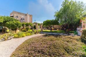 A garden with a pathway, a stone wall, and a building in the background.