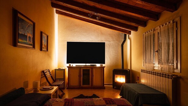 A cozy room with a bed, a desk with a laptop, a television, and a wood-burning stove. - Dependance 'Residence Al Pozzo' with Wi-Fi and Air Conditioning (Capannori)