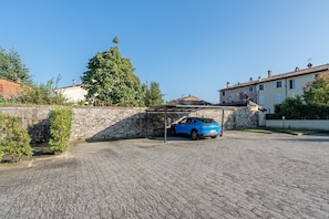 A cobblestone driveway leading to a covered parking area with a blue car parked inside.