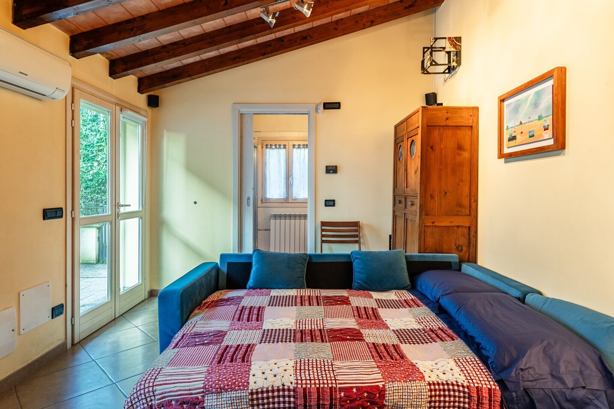 Un dormitorio con una cama grande, un armario de madera, una puerta que da a otra habitación y una ventana con vistas a zonas verdes.