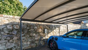 A blue car parked under a covered area with a stone wall and a power outlet. - Dependance 'Residence Al Pozzo' with Wi-Fi and Air Conditioning (Capannori)