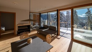 A modern interior with a dining area, sofa, and large windows offering a snowy mountain view.