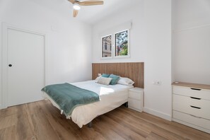 Ein Schlafzimmer mit Bett, Nachttischen, einem Holzkopfende, einem Fenster mit Blick und einem Deckenventilator.