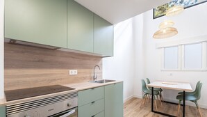 Una cocina moderna con estufa integrada, armarios verdes, encimera de madera y un comedor con mesa y sillas.