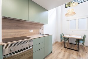 A modern kitchen with a built-in stove, green cabinets, a wooden countertop, and a dining area with a table and chairs.