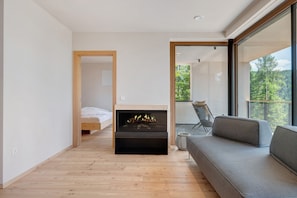 Une chambre moderne dotée d’une cheminée, d’un canapé et d’un balcon offrant une vue sur les arbres.
