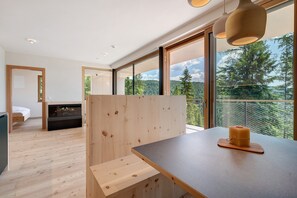 Une chambre moderne avec un plancher en bois, un lit, une cheminée et de grandes fenêtres donnant sur des arbres et un lac.