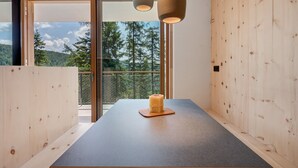 A modern interior with a wooden table, a candle, and a view of trees through a glass door.