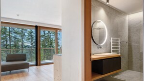 A modern bathroom with a large mirror, a wooden vanity, and a view of trees through large windows.