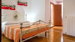 Una cama con estructura metálica, una colcha a rayas y dos cuadros colgados en la pared.