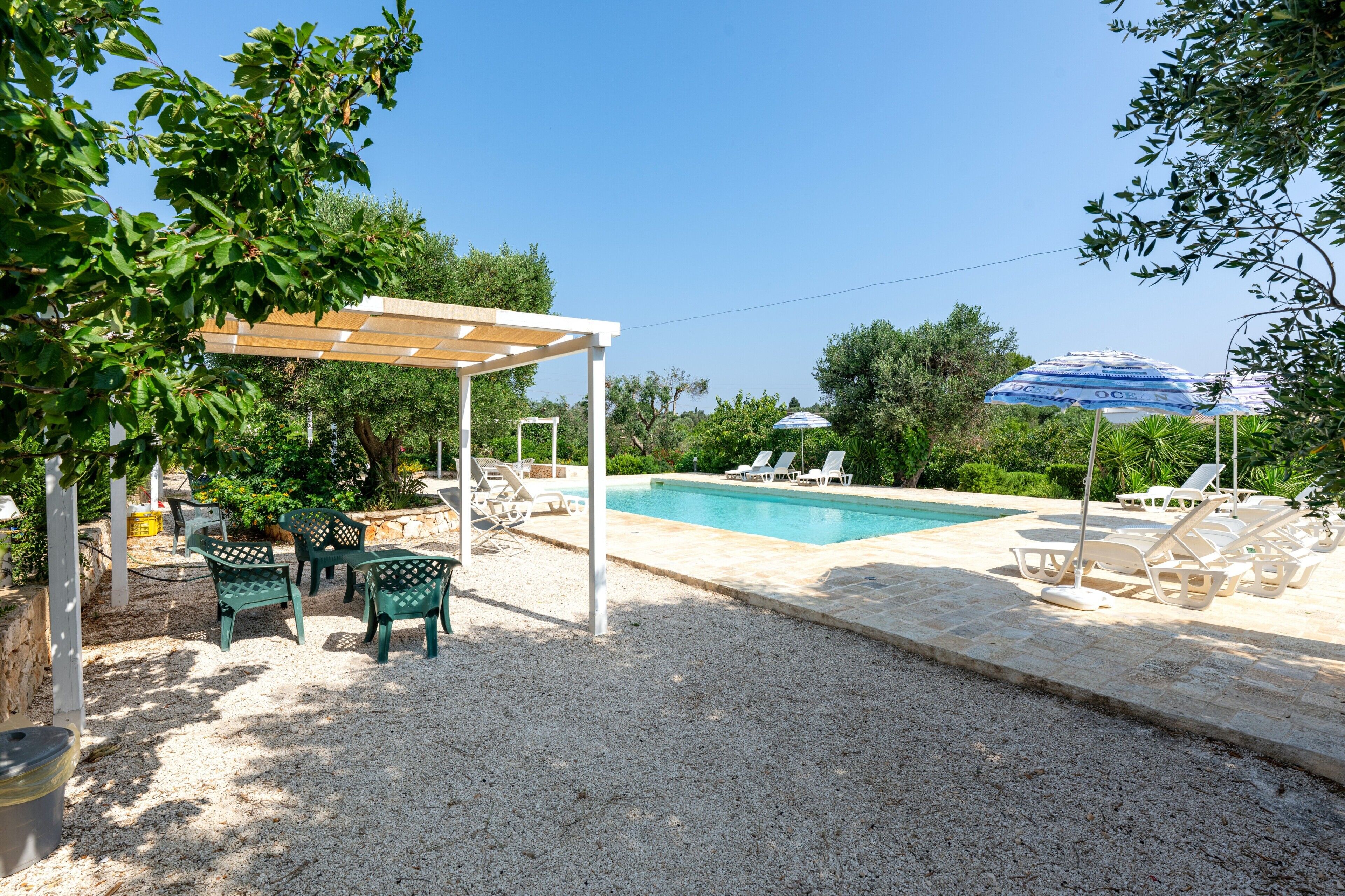 A pool area with lounge chairs, a pergola, and umbrellas.