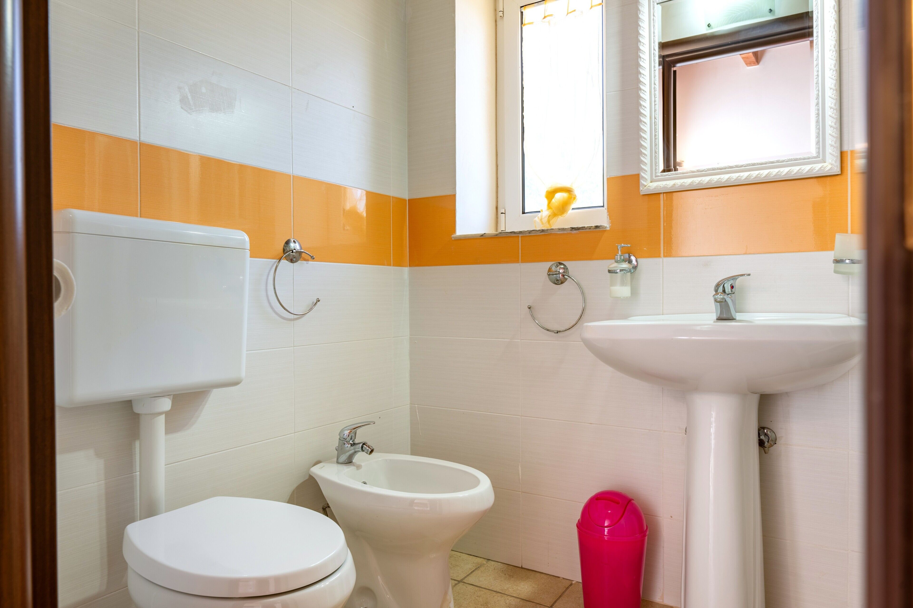 Ein Badezimmer mit Toilette, Bidet, Waschbecken und einem Fenster, an dem ein Handtuch hängt.