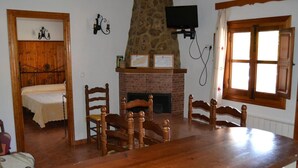 Una stanza con un tavolo da pranzo in legno, sedie, un camino, un televisore montato a parete e un letto con testiera in legno.