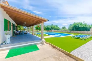 Un espacio al aire libre cubierto con piscina, césped artificial verde y sillones de descanso.