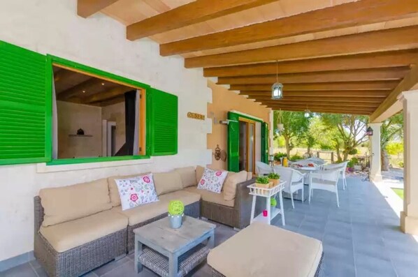 Un patio al aire libre con un sofá, sillas, una mesa y un área de estar cubierta.