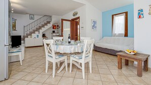 Un comedor con una mesa redonda, sillas y una pequeña mesa de madera con fruta.