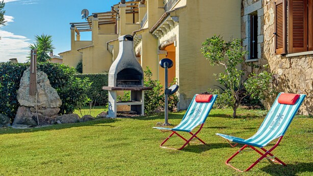 Un edificio de piedra con chimenea de piedra, dos sillones a rayas y un césped bien cuidado.