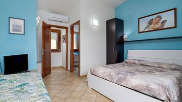 A bedroom with a bed, a television, a door leading to another room, and a wall-mounted air conditioner.
