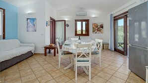 Un espacio habitable compacto con zona de comedor, un sofá, un refrigerador y vista a través de un ventanal.