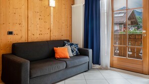 Een kamer met een donkergrijze bank, houten paneelwanden, een radiator en uitzicht door een glazen deur.