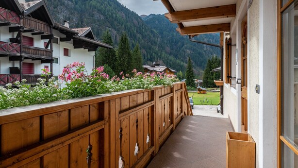 Een houten balkon met uitzicht op een berglandschap, een houten hek en een gebouw met een schuin dak.