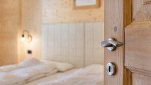 Een houten deur met een sleutelgat en een deurklink, een bed met wit beddengoed, en een wandlamp.