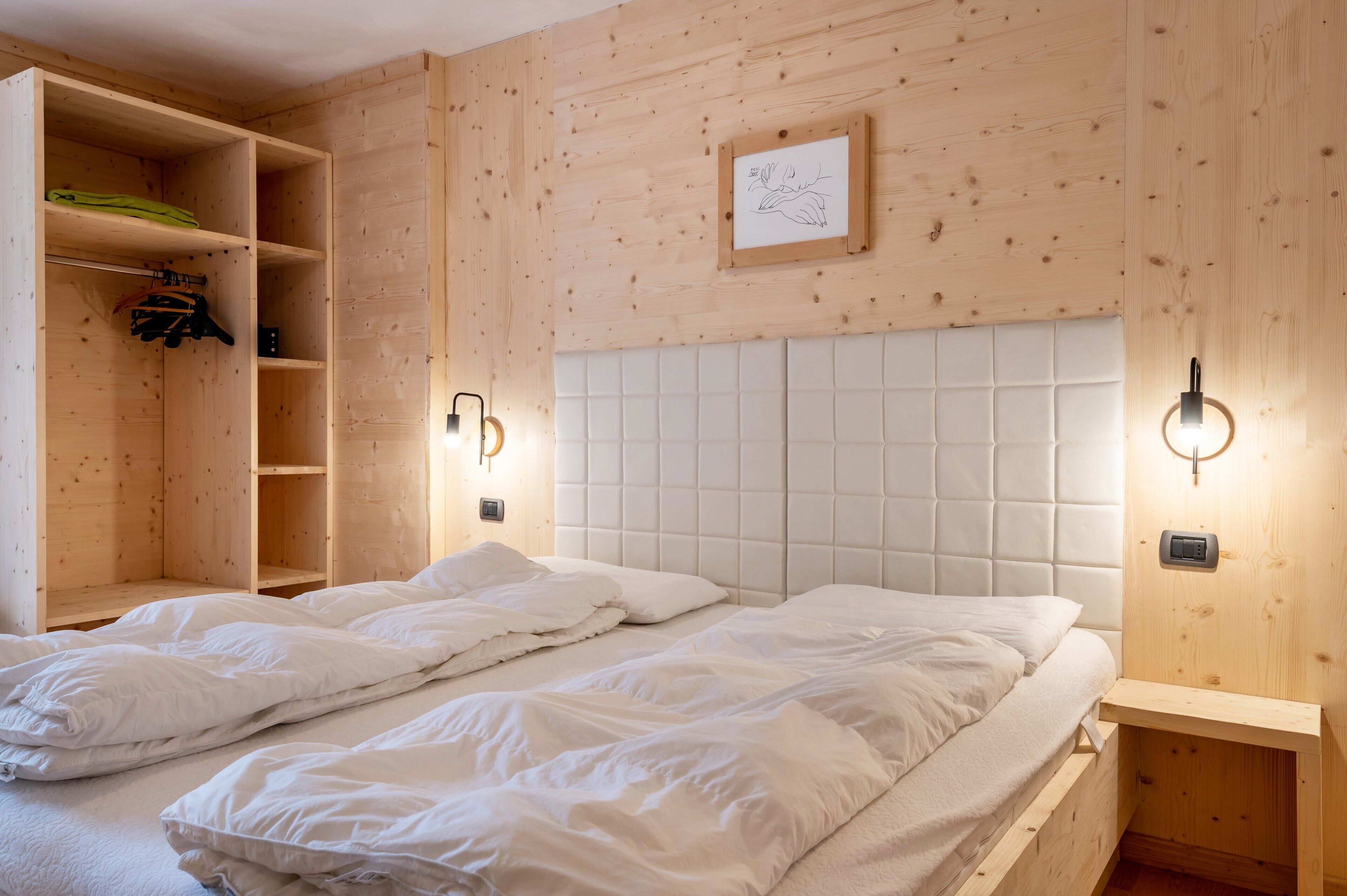 Une chambre avec un lit, une armoire en bois et des lampes fixées au mur.