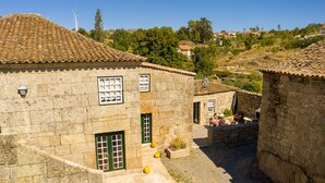 A stone building with a tiled roof, a small courtyard with a table and chairs, and a view of a hilly landscape in the background. - Holiday Home 'Casa Da Cerca' with Mountain View, Wi-Fi and Air Conditioning (Sortelha)
