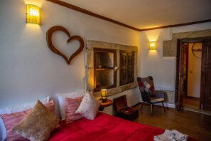 Een kamer met een rode bed, een hartvormige decoratie aan de muur, een houten stoel en een kleine tafel met een lamp.