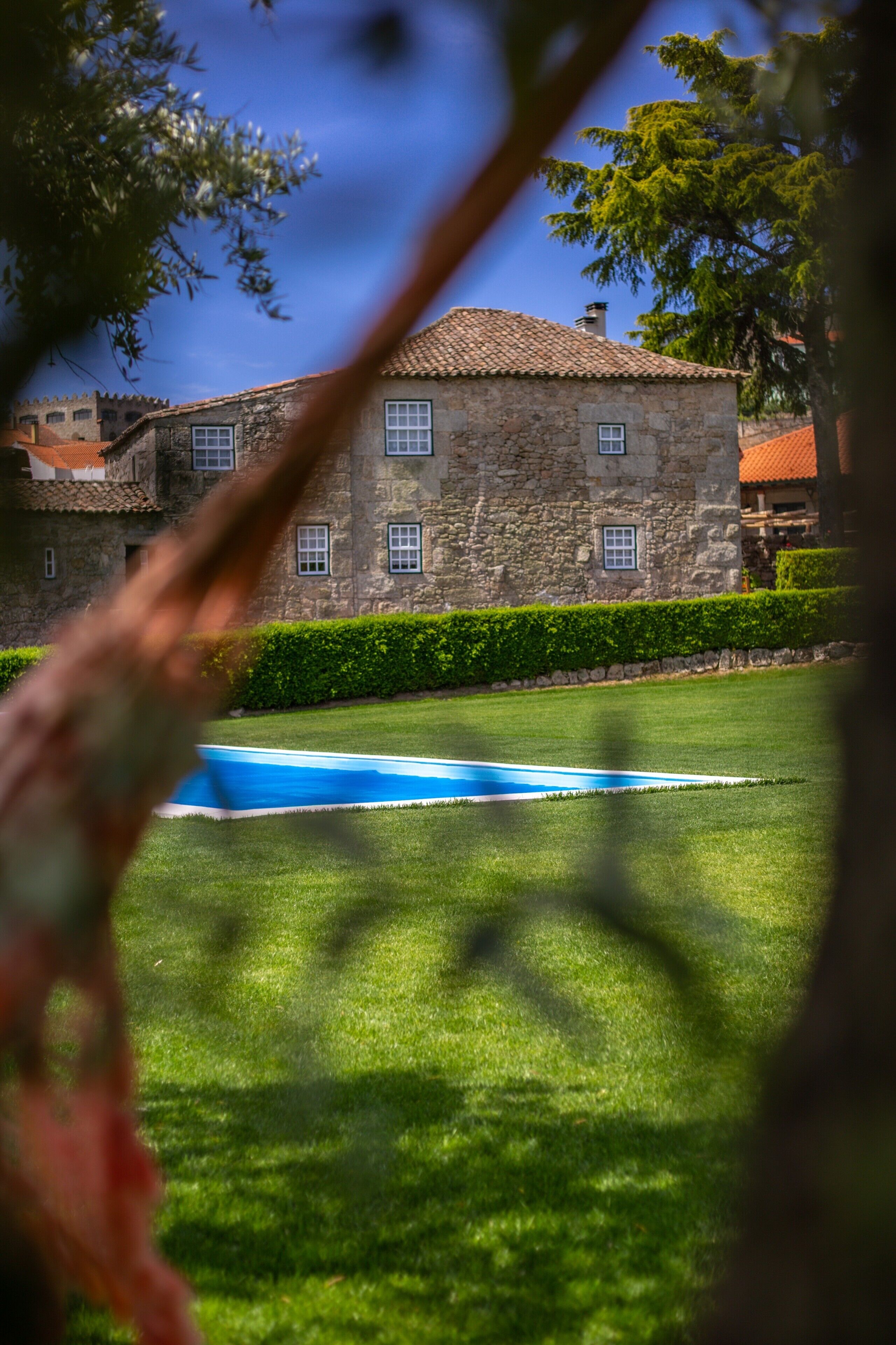 Un bâtiment en pierre avec un toit en tuiles, une piscine et une pelouse bien entretenue.