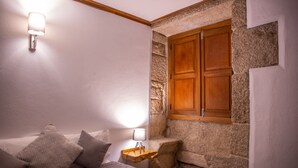 A bedroom with a bed, pillows, a nightstand with a lamp, a wooden wardrobe, and a stone wall. - Holiday Home 'Casa Da Cerca' with Mountain View, Wi-Fi and Air Conditioning (Sortelha)