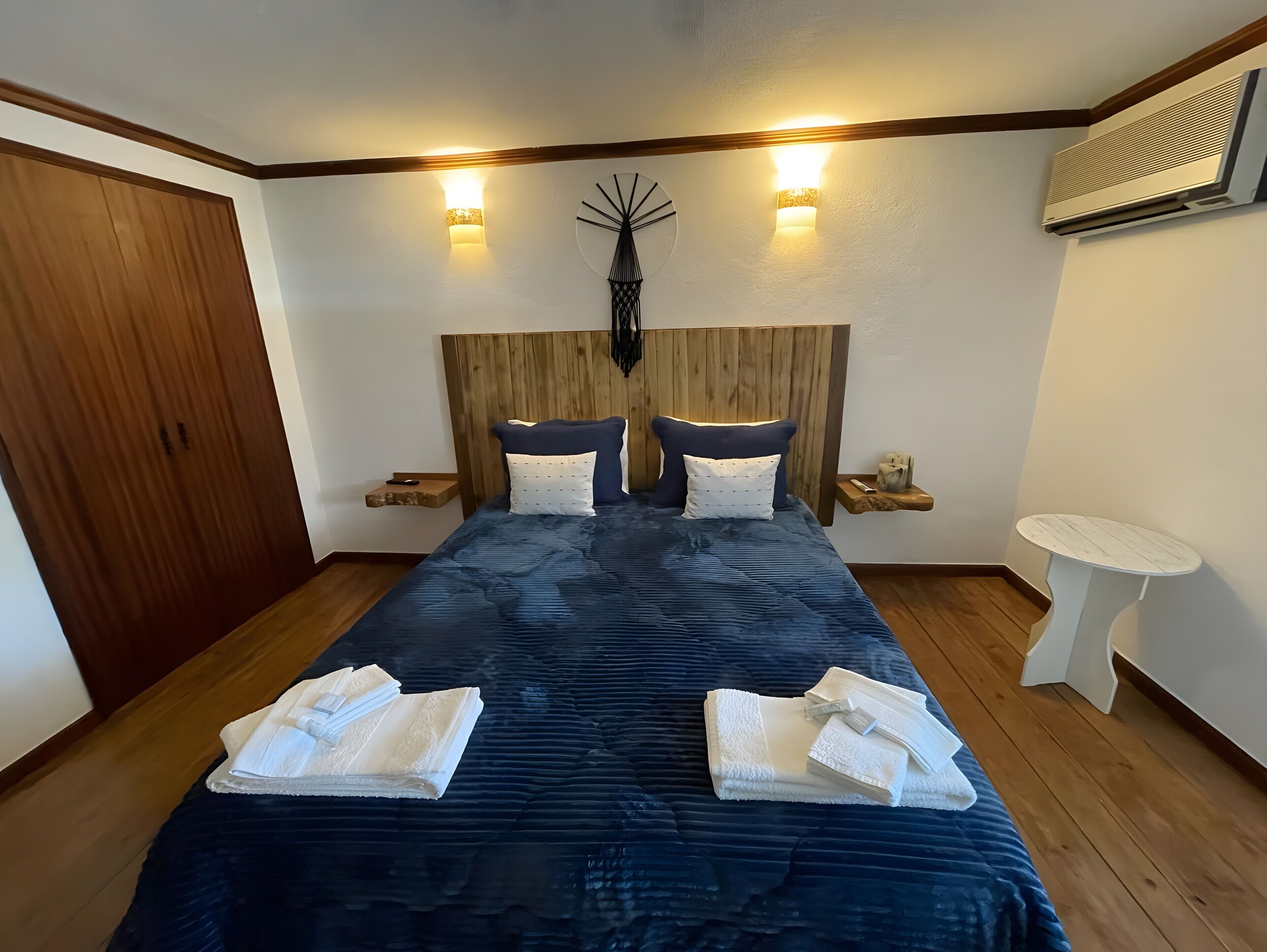 A bedroom with a large bed, bedside tables, a wall-mounted air conditioner, and a small round table.