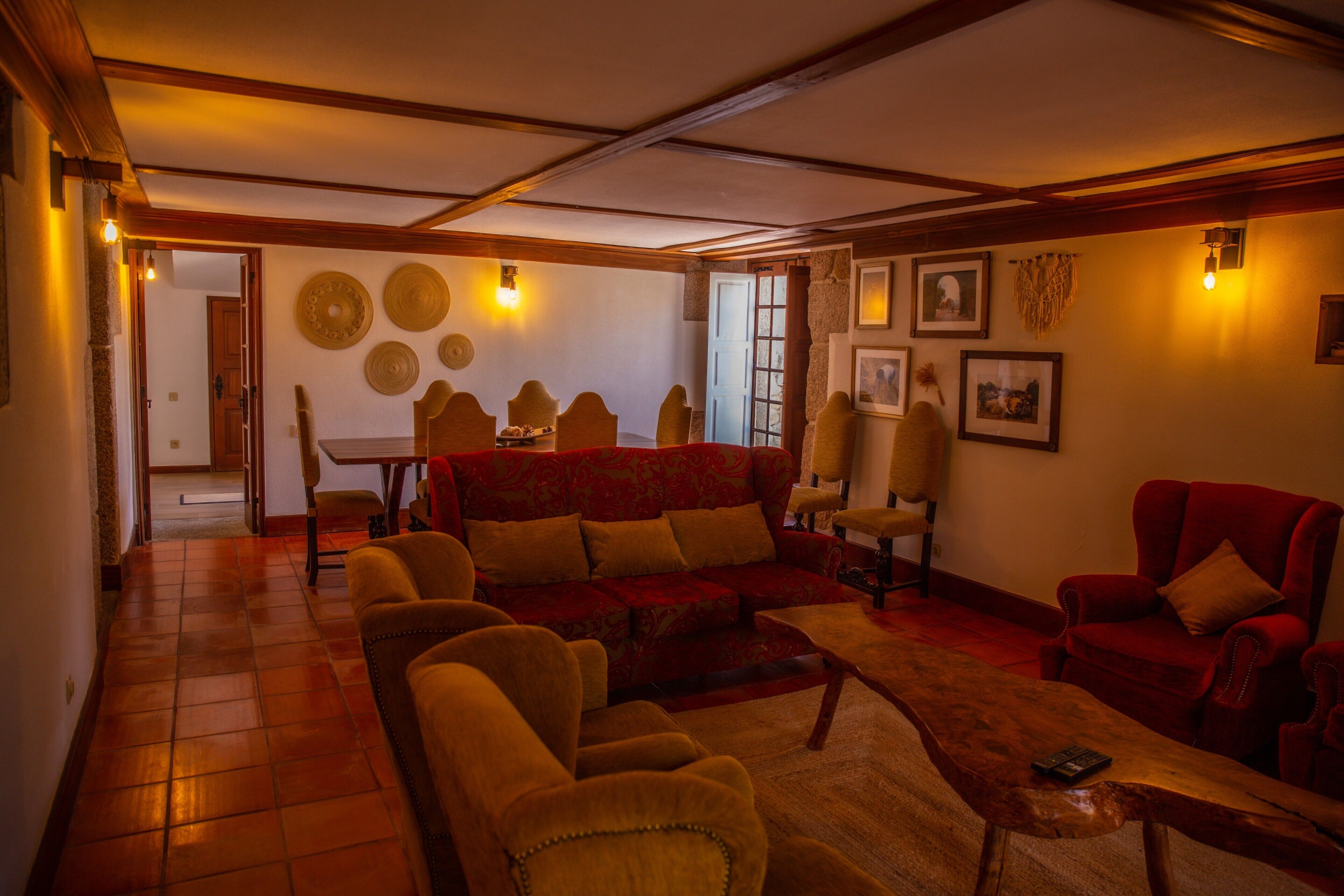 A living room with a red sofa, beige armchairs, a wooden coffee table, and a dining area with a table and chairs.