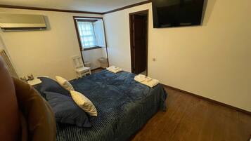 A bedroom with a bed, a chair, a desk, a window, and a TV mounted on the wall.