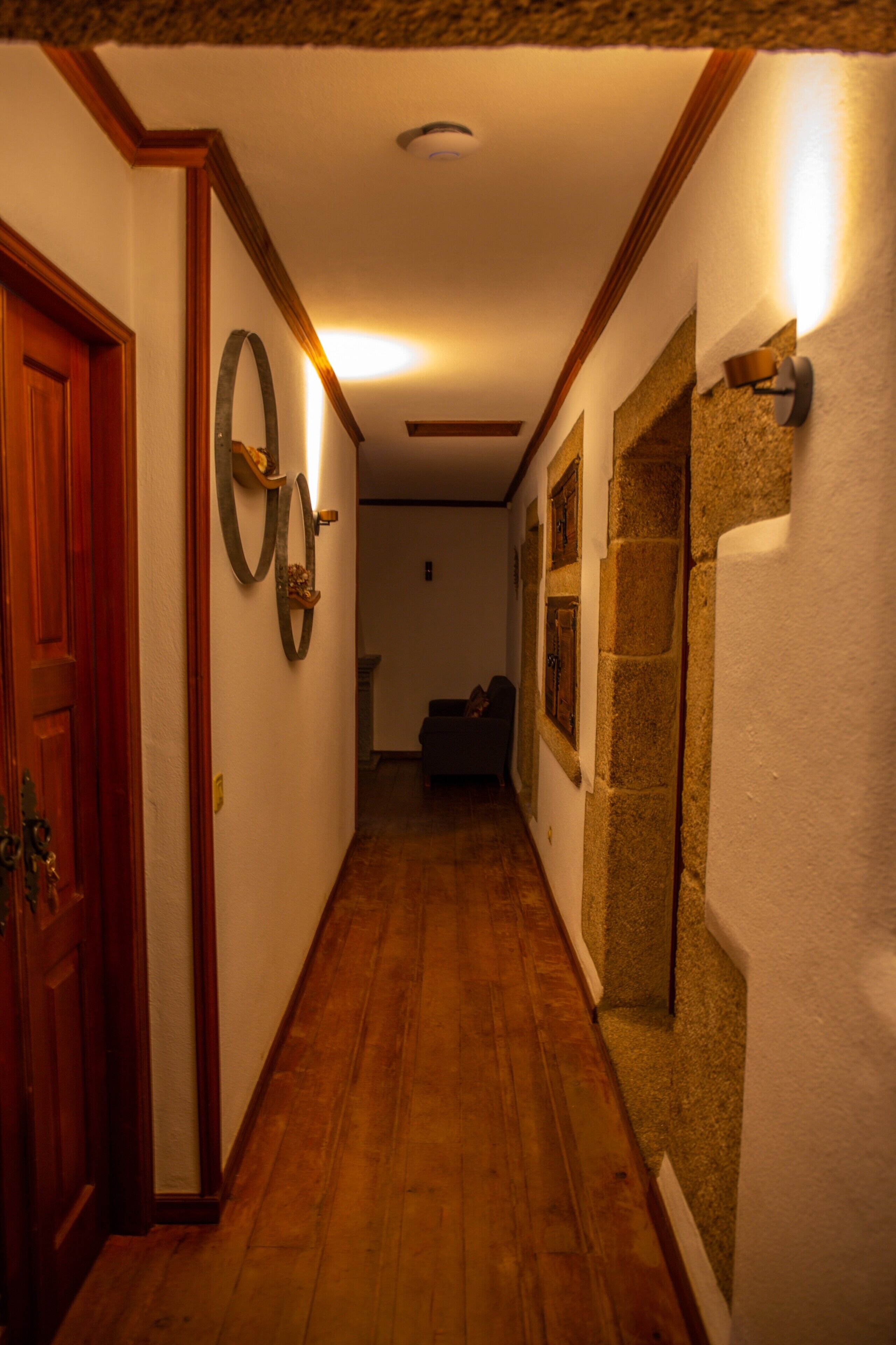 Un pasillo con piso de madera, una puerta de madera, un espejo fijado a la pared y una sección de pared de piedra.